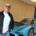 Andreas Schönemann steht lächelnd vor einem futuristischen blauen Elektro-Concept-Car in einem Showroom mit Holzverkleidung.