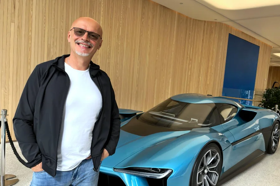 Andreas Schönemann steht lächelnd vor einem futuristischen blauen Elektro-Concept-Car in einem Showroom mit Holzverkleidung.